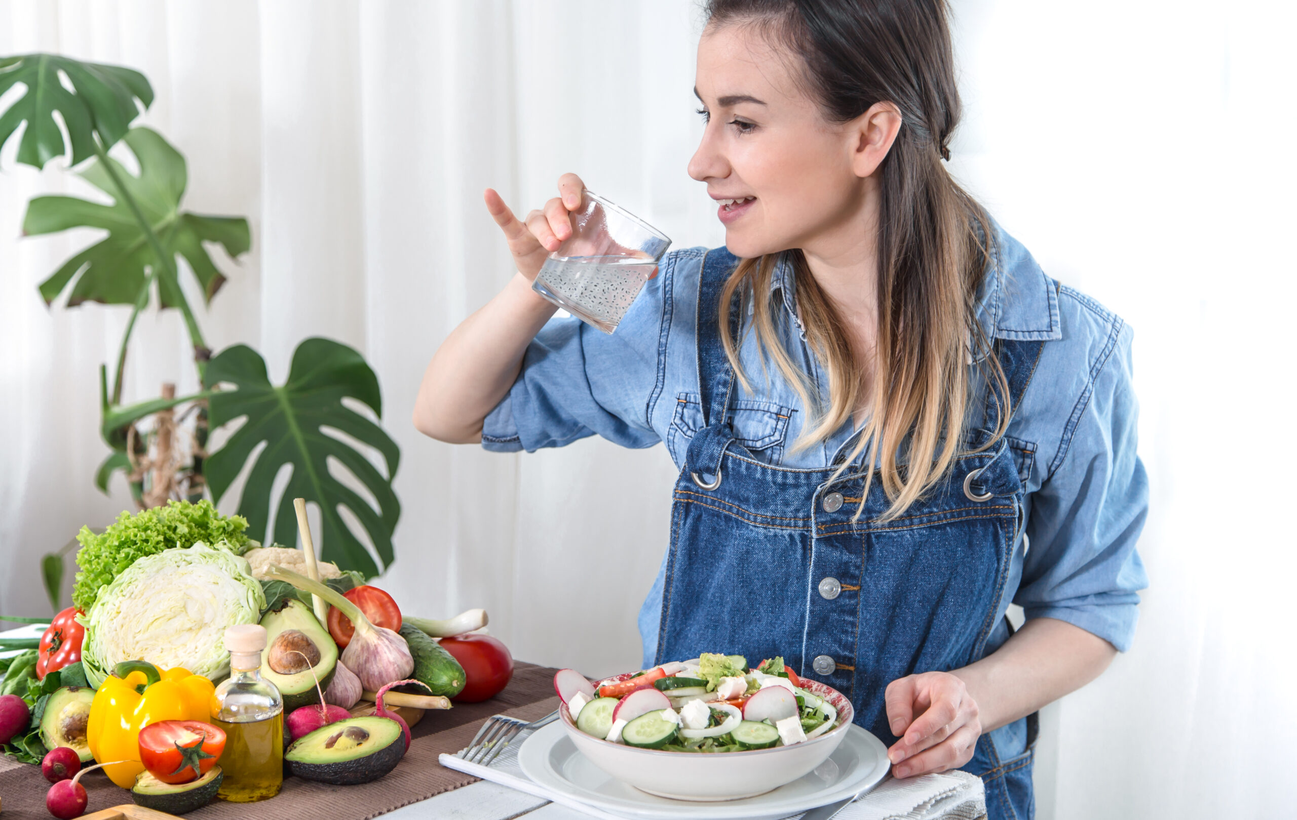 Young woman drinking water at the table with vegetables